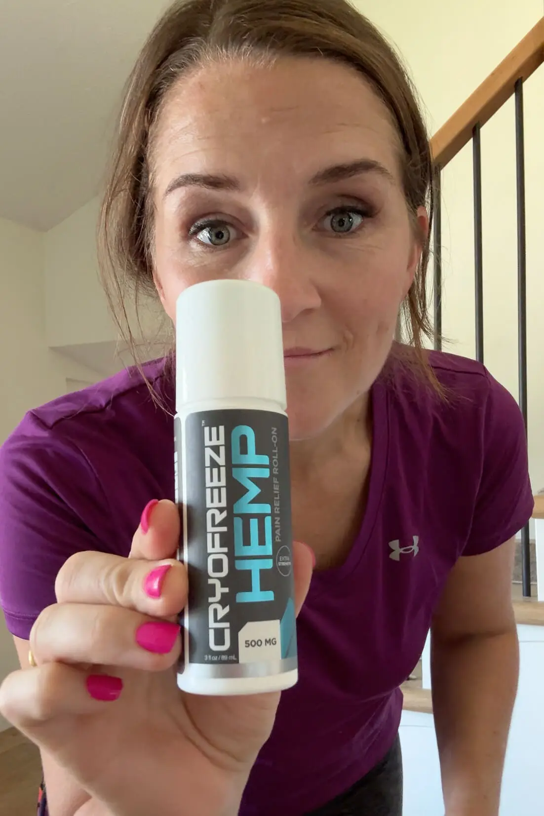 Smiling woman holding CryoFreeze Hemp Pain Relief Roll-On, a natural remedy for soreness and inflammation.